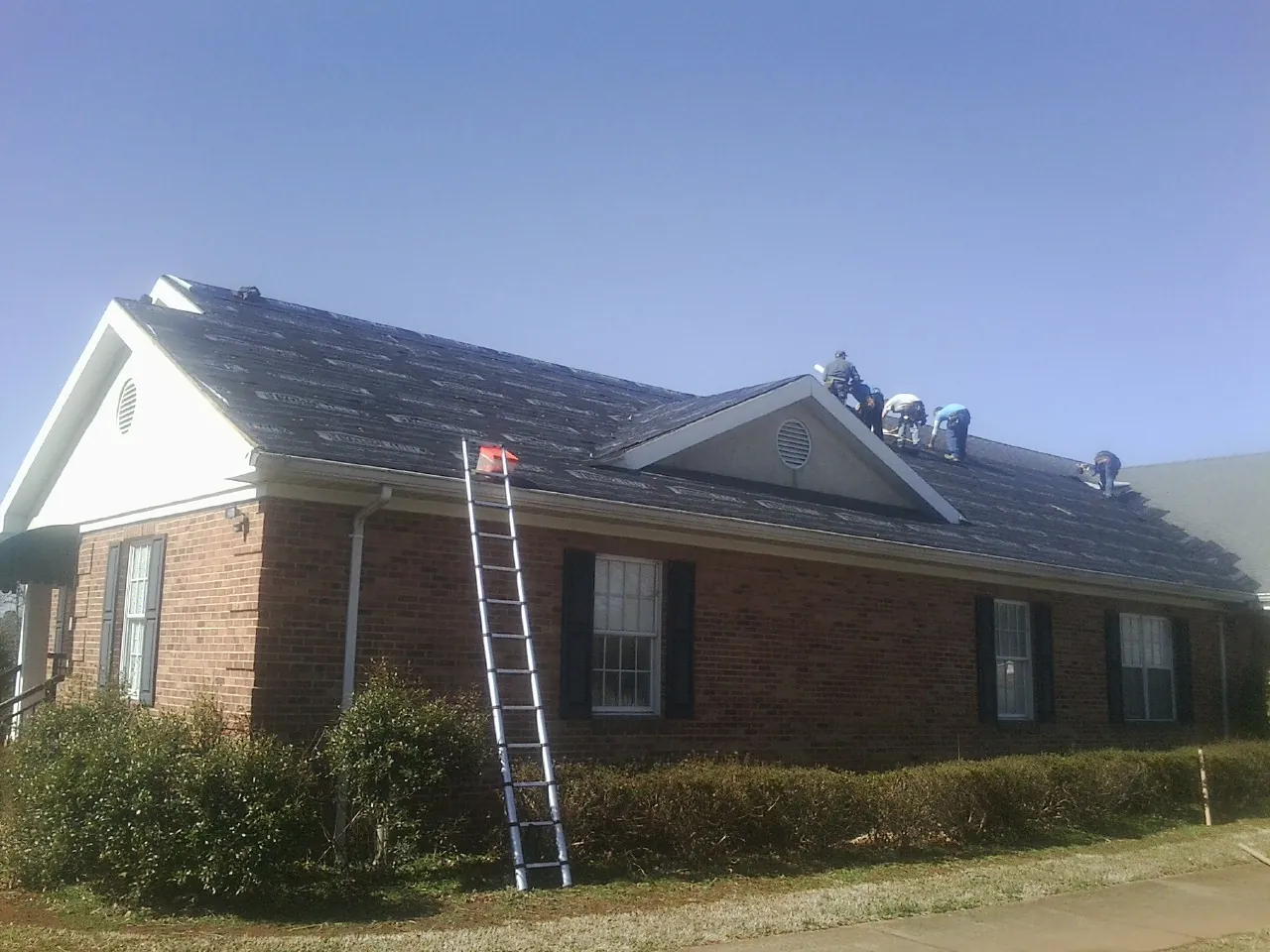 Crew tearing shingles off a brick ranch roof with a ladder set — Emergency Roof Repair work by our crew in Danevang