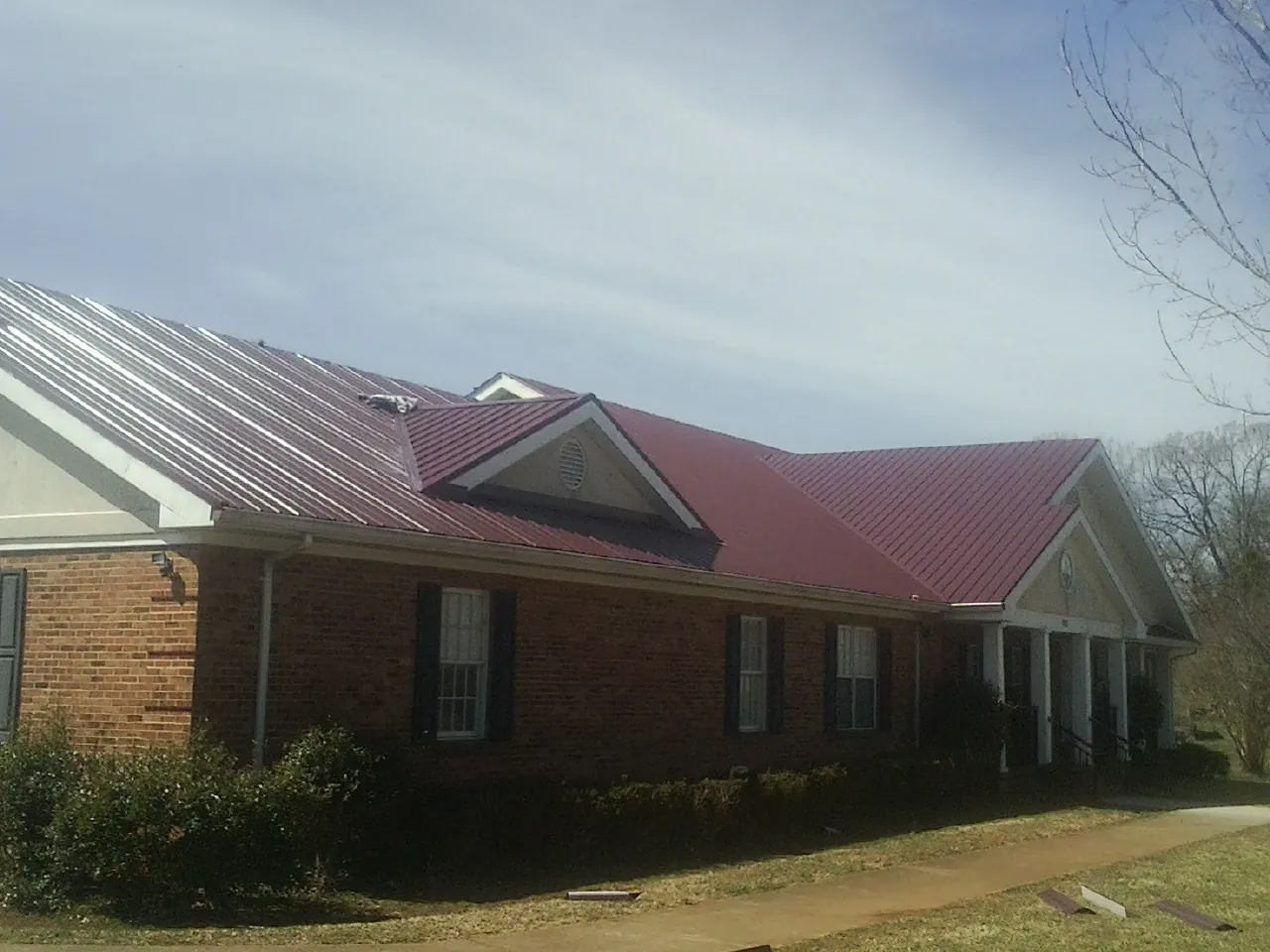 Red metal roof with gabled entries on a long brick building, from a Hail Damage Roof Repair job in Danevang