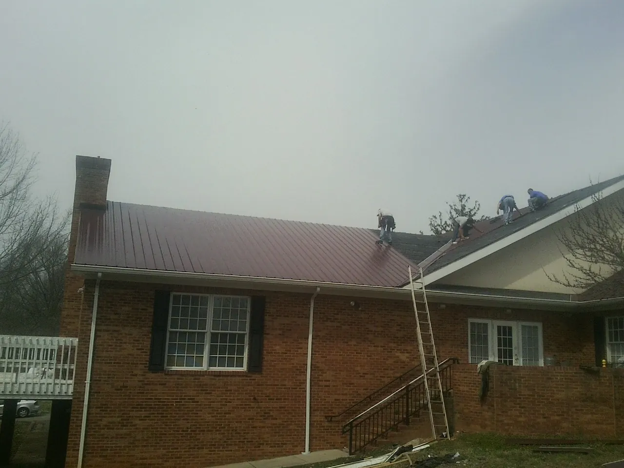 Crew setting red metal roofing panels on a brick home in Danevang