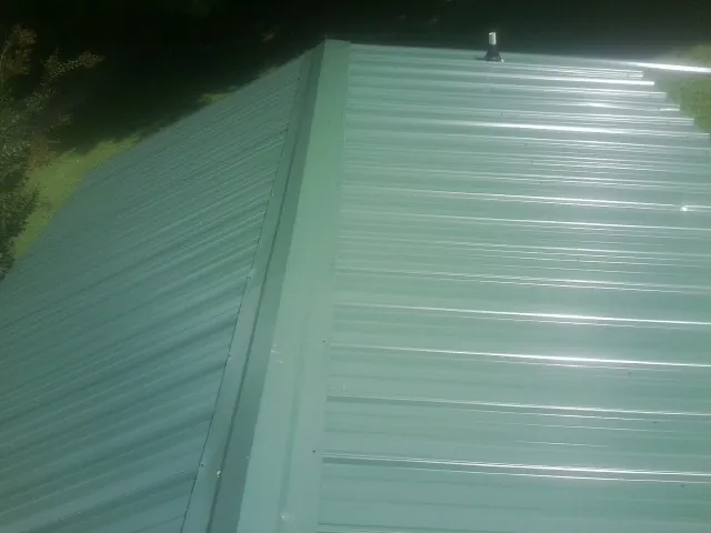 New green metal panels meeting at the ridge of a roof — Flat Roof Repair work by our crew in Danevang